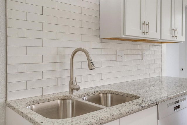 kitchen with decorative backsplash, white cabinetry, a sink, light stone countertops, and dishwasher