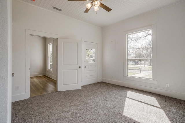 unfurnished bedroom with baseboards, visible vents, ceiling fan, crown molding, and carpet flooring