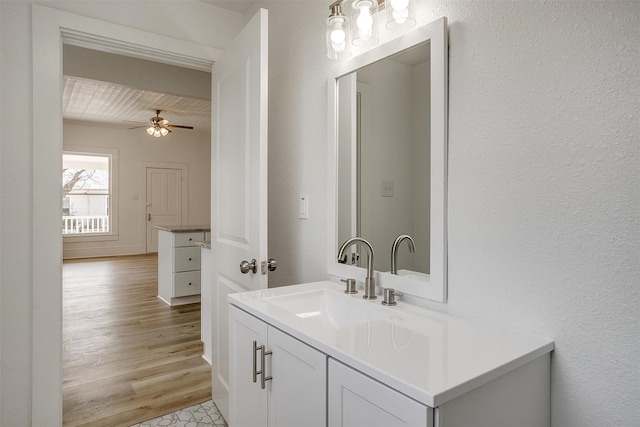 bathroom featuring ceiling fan, a textured wall, wood finished floors, and vanity