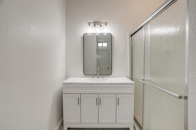 bathroom with a textured wall, a shower with door, and vanity