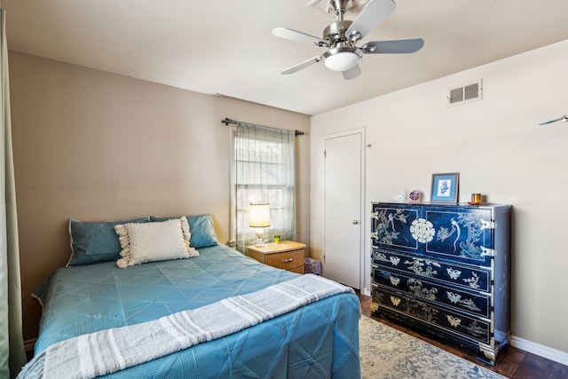 bedroom with a ceiling fan, visible vents, baseboards, and wood finished floors