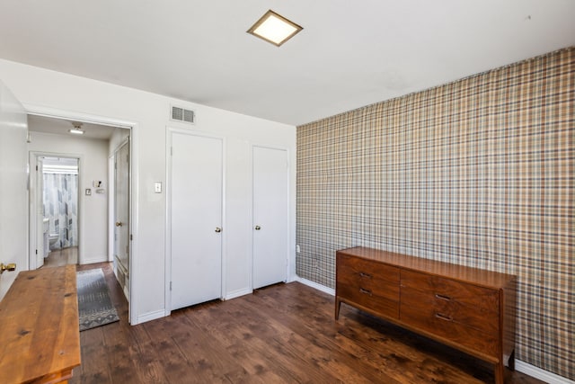 unfurnished bedroom featuring wallpapered walls, wood finished floors, visible vents, and baseboards