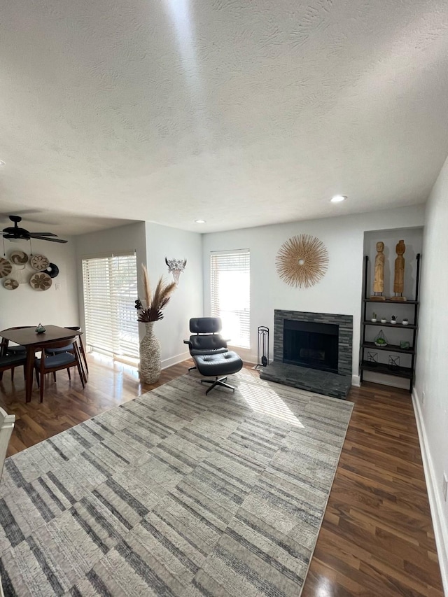 living room featuring recessed lighting, a fireplace with raised hearth, baseboards, and wood finished floors