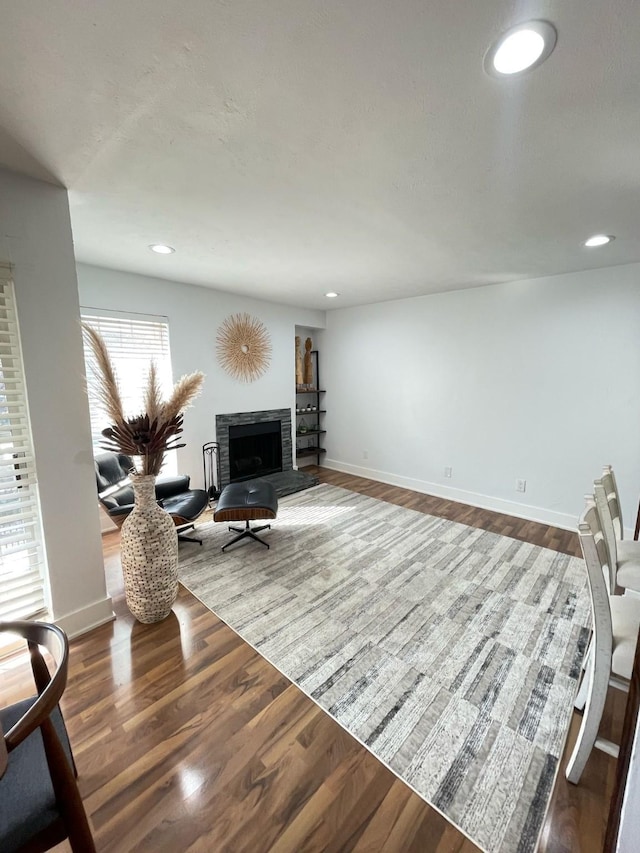 living room with a fireplace with raised hearth, baseboards, and wood finished floors