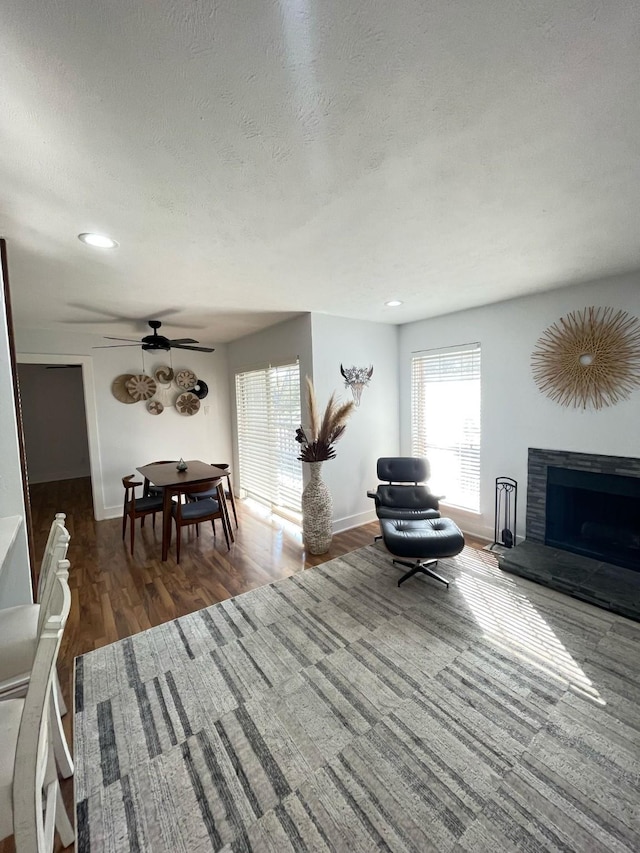 living room featuring a fireplace with raised hearth, a textured ceiling, wood finished floors, and baseboards