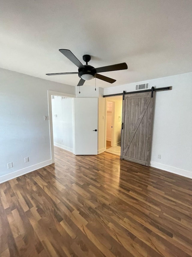 empty room featuring a barn door, visible vents, dark wood finished floors, and baseboards