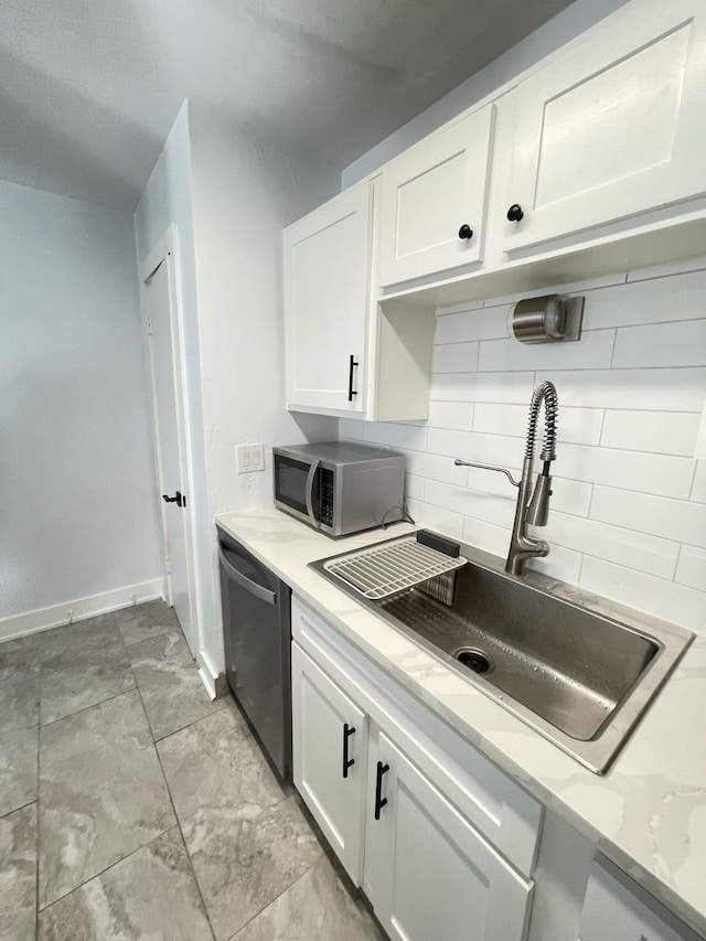 kitchen featuring stainless steel appliances, backsplash, white cabinets, a sink, and baseboards