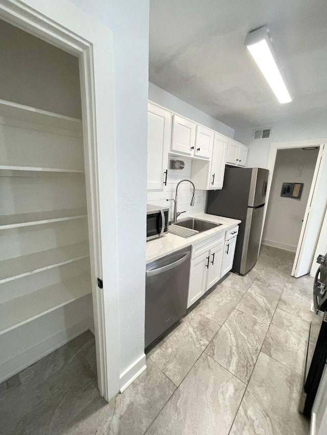 kitchen featuring stainless steel appliances, a sink, visible vents, white cabinets, and backsplash