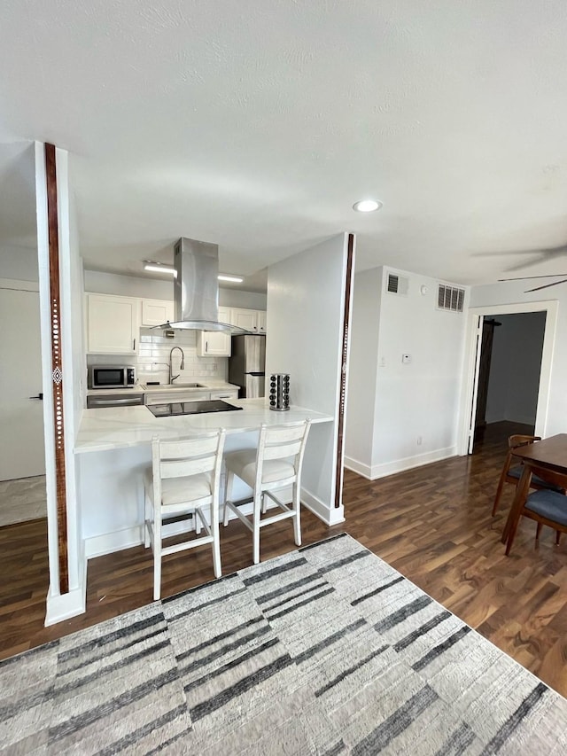 kitchen featuring island range hood, stainless steel appliances, visible vents, decorative backsplash, and dark wood-style floors