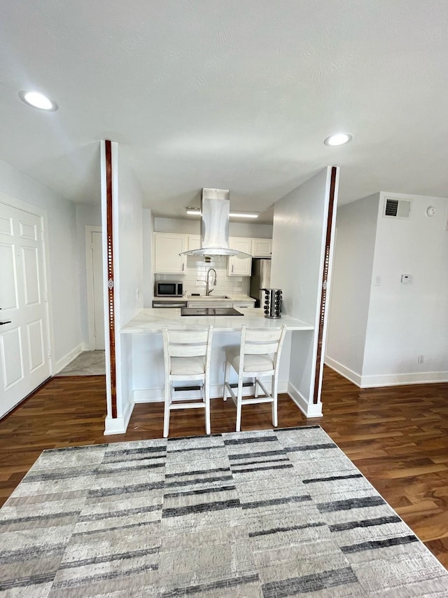 kitchen with visible vents, island range hood, white cabinets, appliances with stainless steel finishes, and wood finished floors