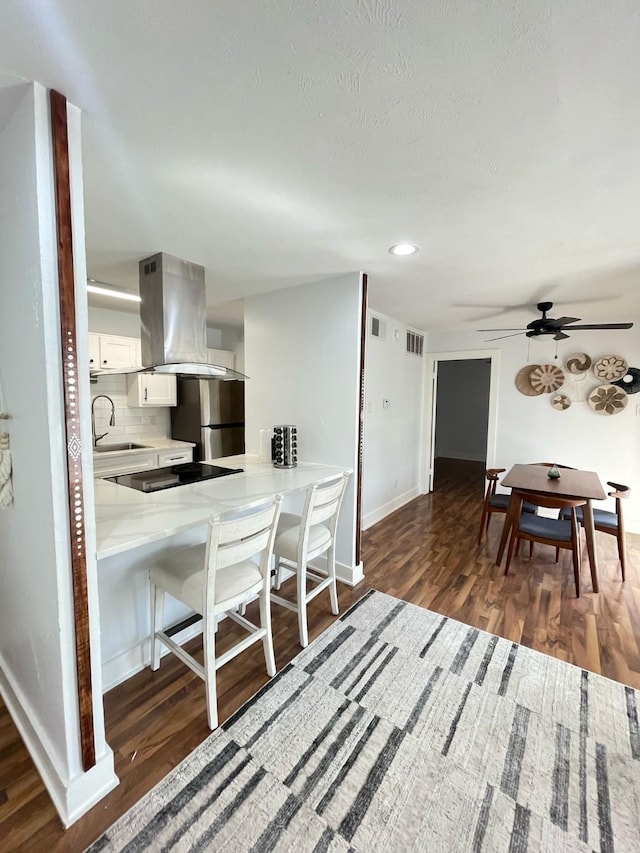 kitchen featuring dark wood finished floors, freestanding refrigerator, island exhaust hood, black electric stovetop, and backsplash