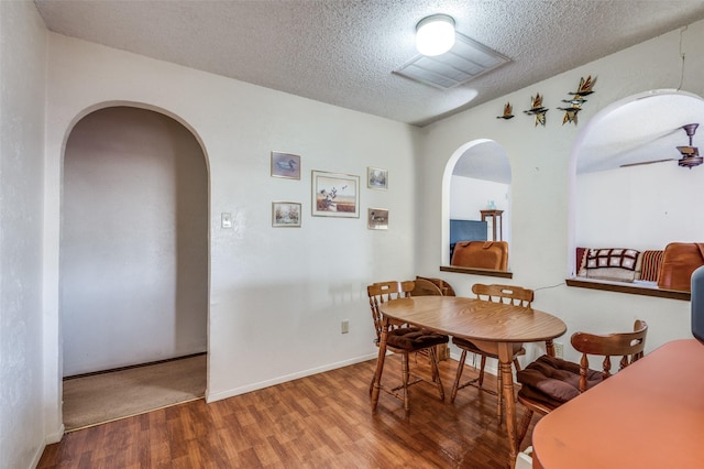 dining area with a textured ceiling, arched walkways, wood finished floors, visible vents, and a ceiling fan