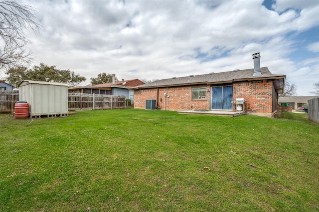 rear view of house with a lawn, a fenced backyard, a storage unit, an outdoor structure, and brick siding