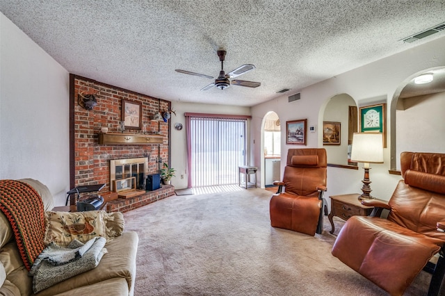 carpeted living room with a textured ceiling, a fireplace, visible vents, and a ceiling fan