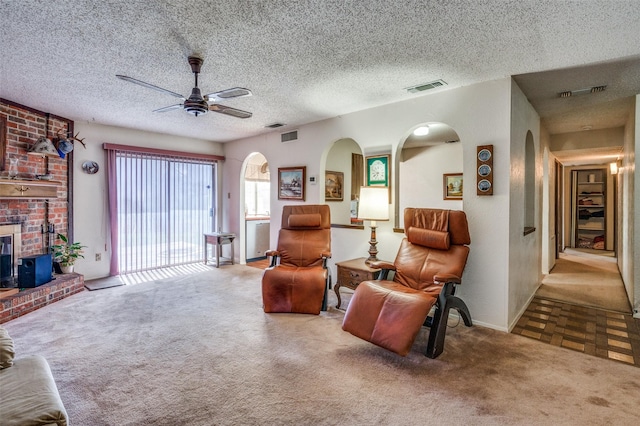 living area featuring carpet floors, a brick fireplace, visible vents, and a ceiling fan