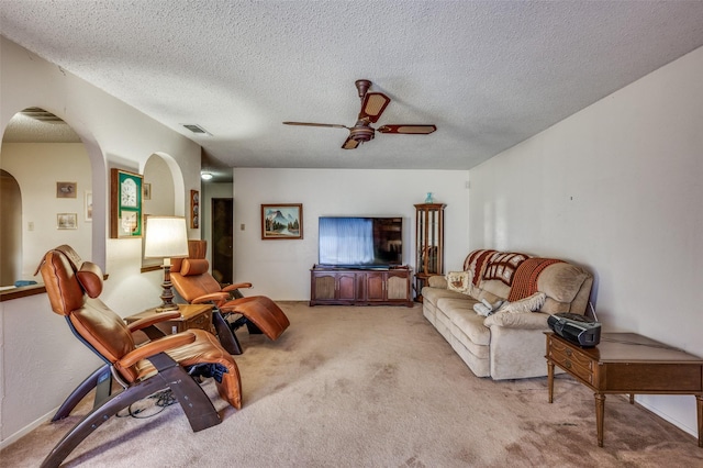 carpeted living room featuring ceiling fan, visible vents, arched walkways, and a textured ceiling