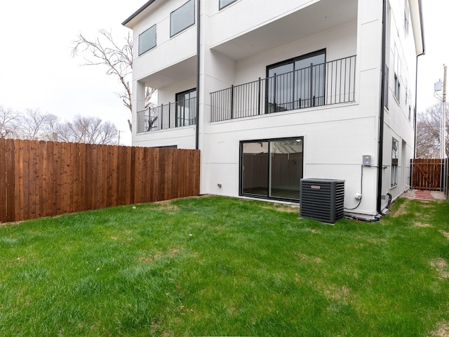 rear view of house with cooling unit, fence, a yard, and stucco siding