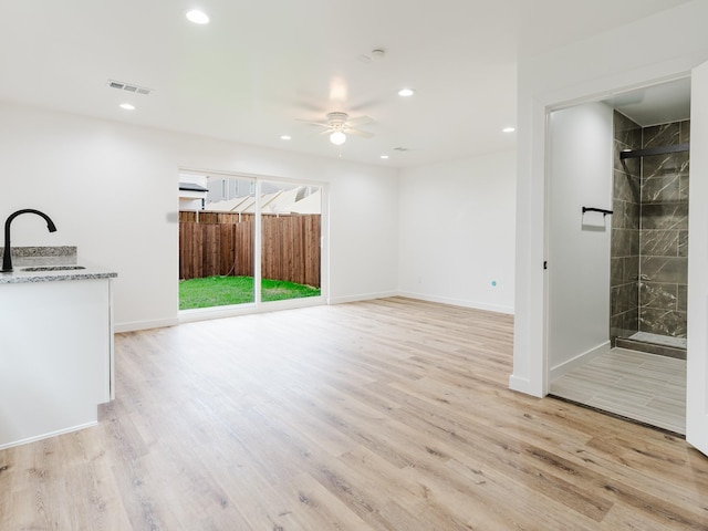 unfurnished living room featuring light wood-type flooring, ceiling fan, and a sink