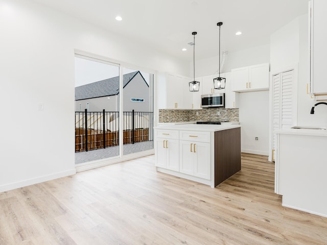 kitchen featuring a sink, stainless steel microwave, backsplash, white cabinets, and light countertops