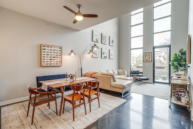 dining area with baseboards, a ceiling fan, a towering ceiling, expansive windows, and concrete flooring