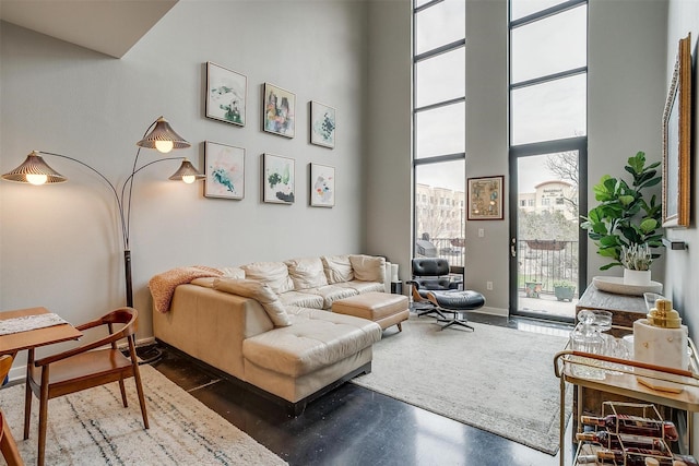 living room featuring a towering ceiling, baseboards, a wall of windows, and concrete flooring