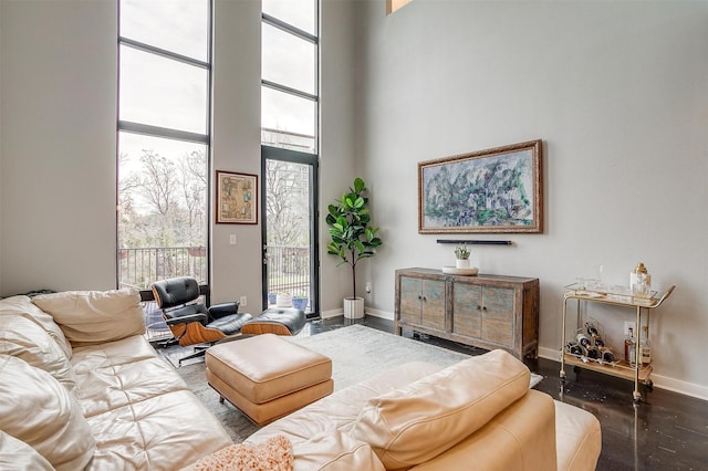 living area featuring a towering ceiling, plenty of natural light, floor to ceiling windows, and baseboards