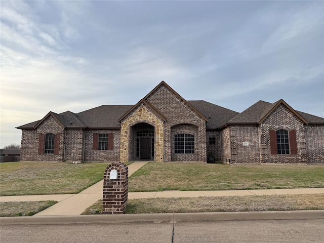 french provincial home featuring brick siding, a front lawn, and roof with shingles