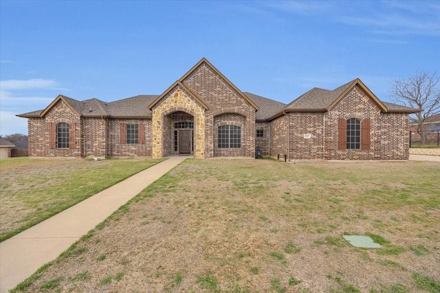 french country style house featuring roof with shingles, brick siding, and a front lawn