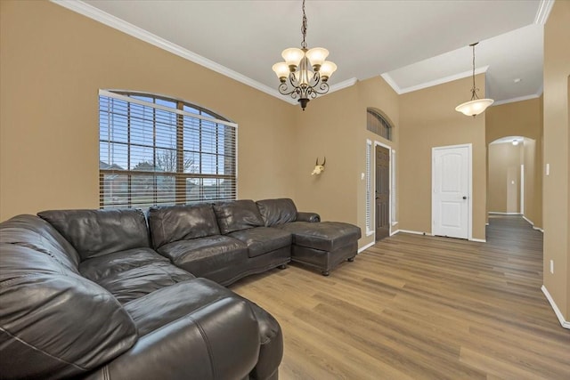 living room featuring arched walkways, a notable chandelier, baseboards, light wood-style floors, and ornamental molding