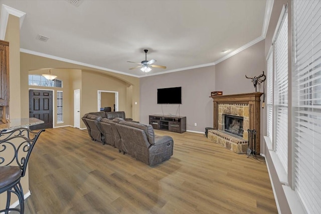 living room featuring crown molding, arched walkways, a fireplace, and light wood finished floors