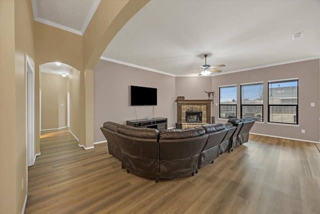 living room with arched walkways, visible vents, a fireplace with raised hearth, and wood finished floors