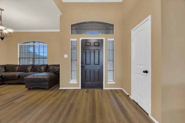 foyer entrance with ornamental molding, a notable chandelier, baseboards, and wood finished floors