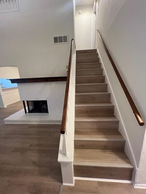 staircase with visible vents, a fireplace, and wood finished floors