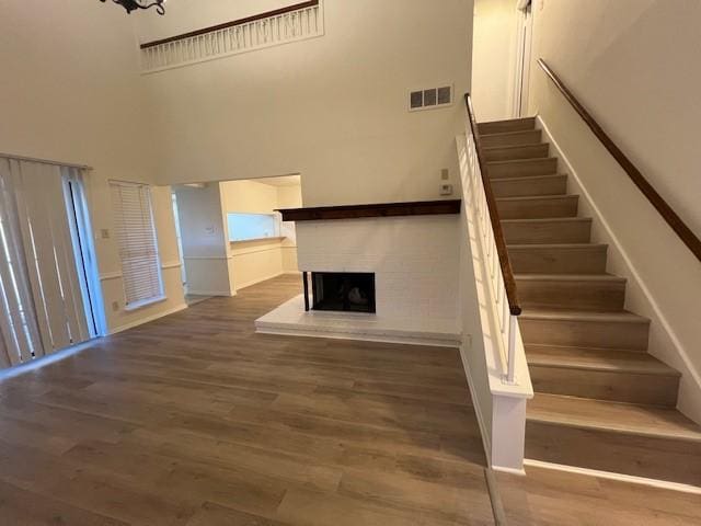 stairway with visible vents, a fireplace with raised hearth, a towering ceiling, and wood finished floors