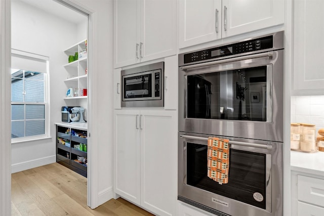 kitchen featuring decorative backsplash, appliances with stainless steel finishes, light countertops, light wood-type flooring, and white cabinetry