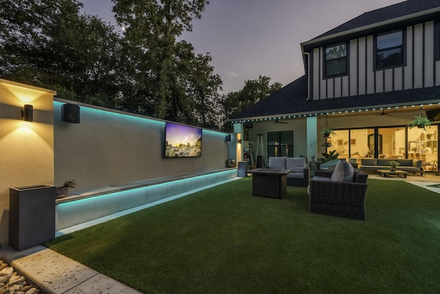 back of property at dusk featuring outdoor lounge area and a lawn