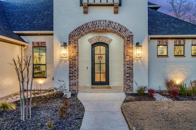 doorway to property with a shingled roof and brick siding