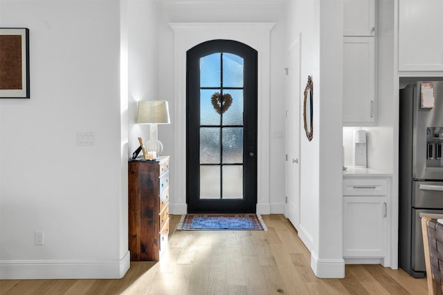 foyer entrance with arched walkways, light wood-type flooring, and baseboards