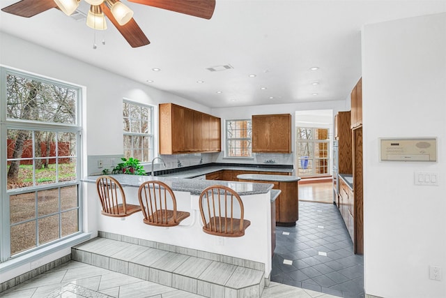 kitchen featuring brown cabinetry, visible vents, a healthy amount of sunlight, and a peninsula