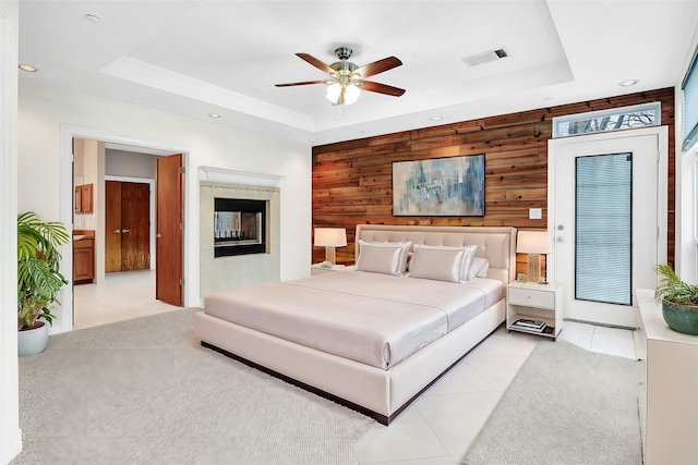 bedroom with visible vents, wood walls, a tray ceiling, light carpet, and a glass covered fireplace