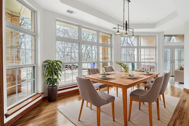 dining space featuring a tray ceiling, french doors, visible vents, and light wood finished floors