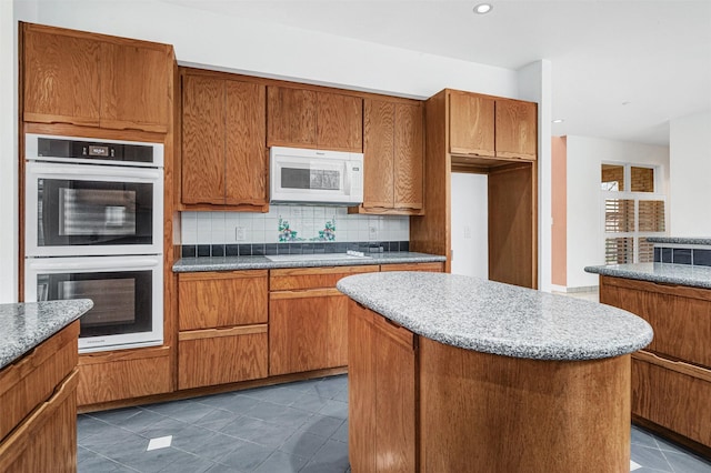 kitchen with brown cabinetry, white appliances, tasteful backsplash, and a center island