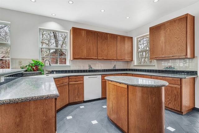 kitchen featuring tasteful backsplash, brown cabinetry, white dishwasher, and a sink