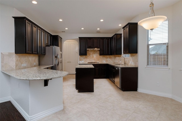 kitchen with light stone countertops, under cabinet range hood, appliances with stainless steel finishes, a peninsula, and a sink