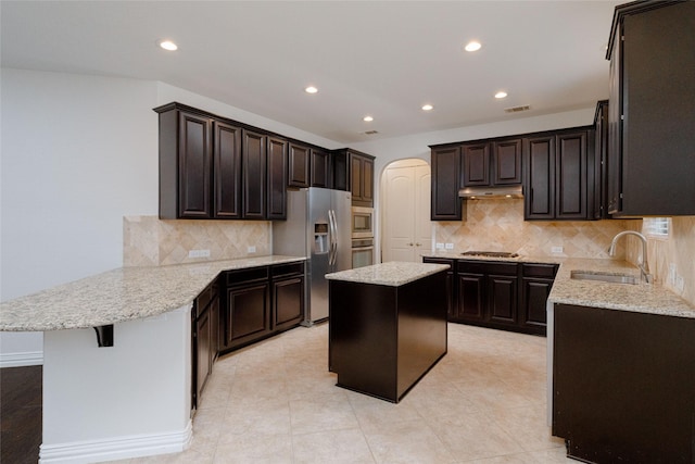 kitchen featuring a peninsula, arched walkways, a sink, under cabinet range hood, and appliances with stainless steel finishes