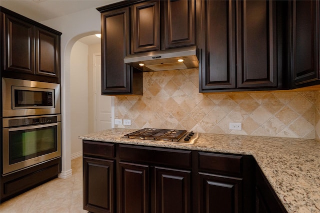 kitchen featuring light tile patterned floors, arched walkways, stainless steel appliances, under cabinet range hood, and tasteful backsplash