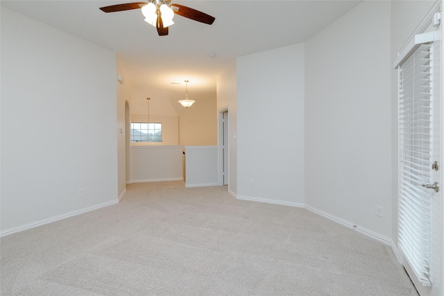 spare room featuring ceiling fan, arched walkways, baseboards, and light carpet