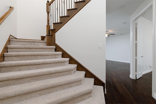 staircase with hardwood / wood-style floors, a ceiling fan, and baseboards