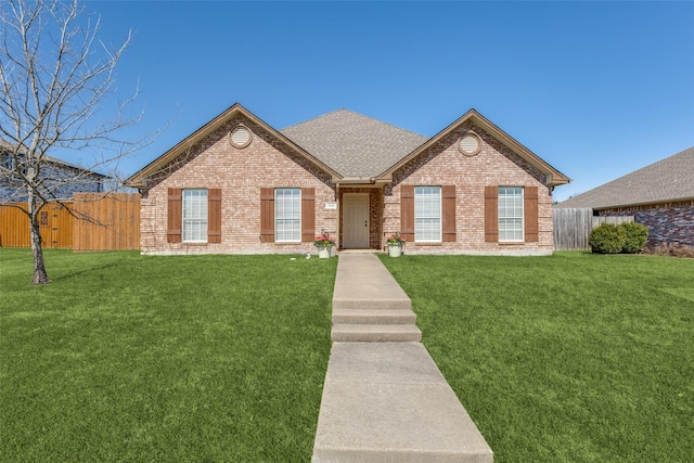 ranch-style home featuring brick siding, roof with shingles, a front yard, and fence