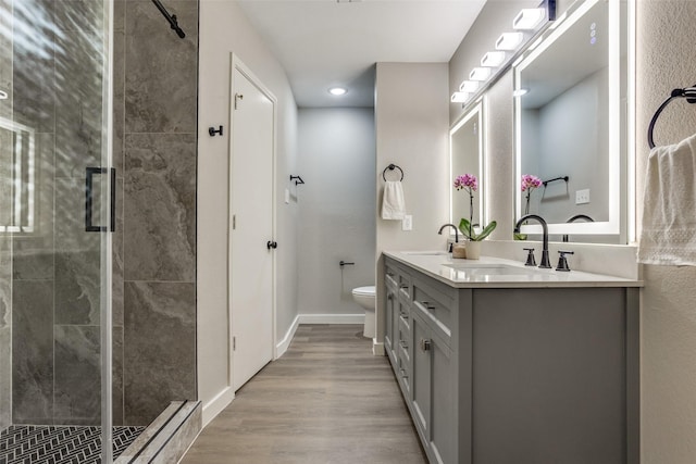 bathroom with toilet, wood finished floors, a stall shower, and a sink